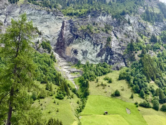 Grüne Almwiesen mit kleinen Häusern vor bewaldeten Felsen und Bergen