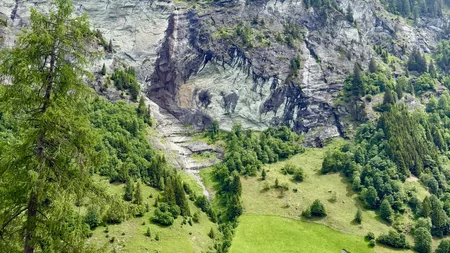 Grüne Almwiesen mit kleinen Häusern vor bewaldeten Felsen und Bergen