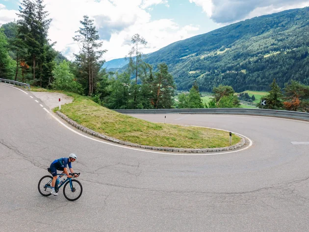 Radfahrer auf kurviger Bergstraße mit grünen Hügeln im Hintergrund