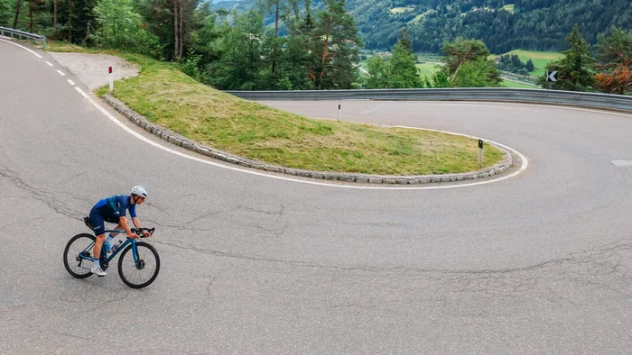 Austria Giro unsupported © Hotel Melodia del Bosco Radfahrer auf kurviger Bergstraße mit grünen Hügeln im Hintergrund