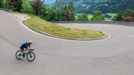 Radfahrer auf kurviger Bergstraße mit grünen Hügeln im Hintergrund