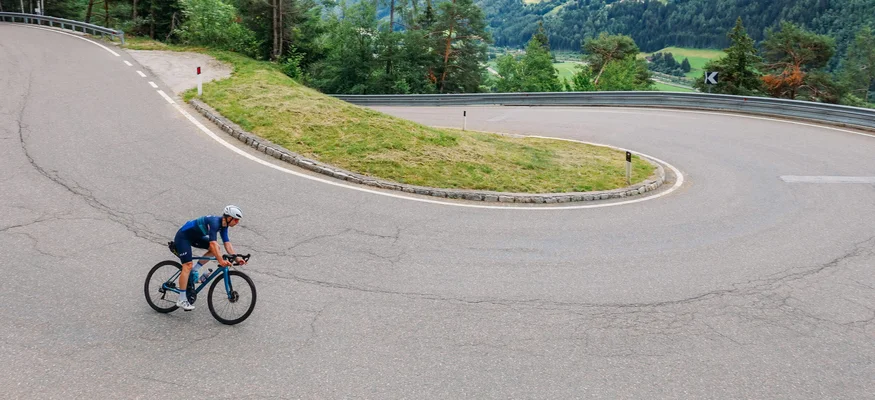 Radfahrer auf kurviger Bergstraße mit grünen Hügeln im Hintergrund