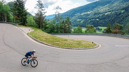 Radfahrer auf kurviger Bergstraße mit grünen Hügeln im Hintergrund