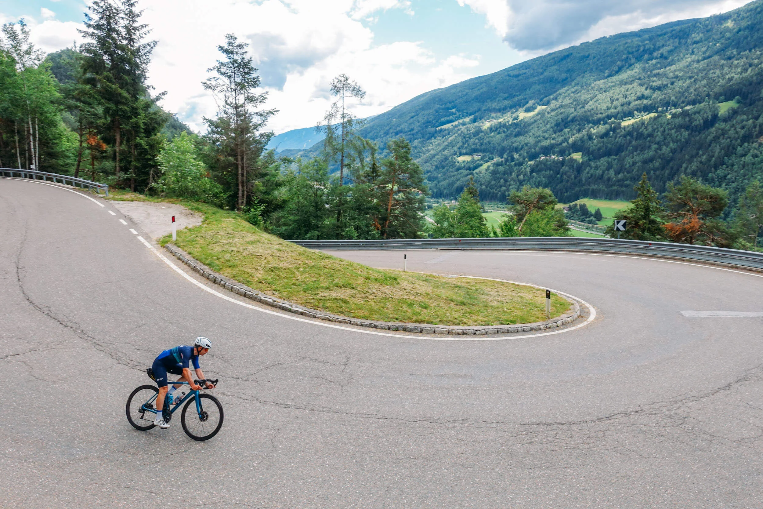 Bikepacking © Hotel Melodia del Bosco Cyclist on winding mountain road with green hills in the background