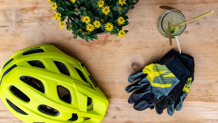 Fahrradhelm, Handschuhe, blühende Pflanze und Getränk auf Holztisch