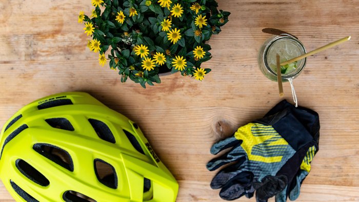 Fahrradhelm, Handschuhe, blühende Pflanze und Getränk auf Holztisch