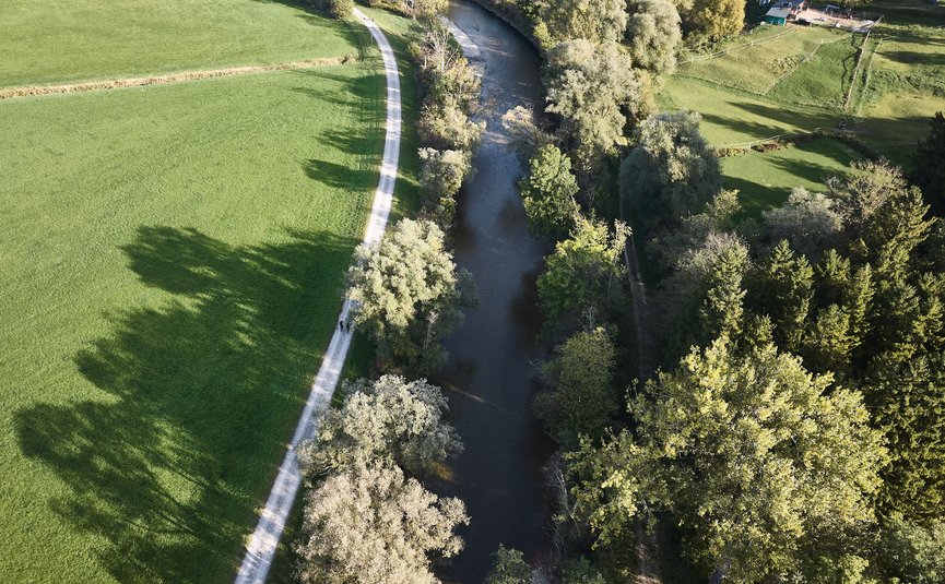 Luftaufnahme eines Flusses mit Bäumen und einem Weg daneben in einer ländlichen Umgebung