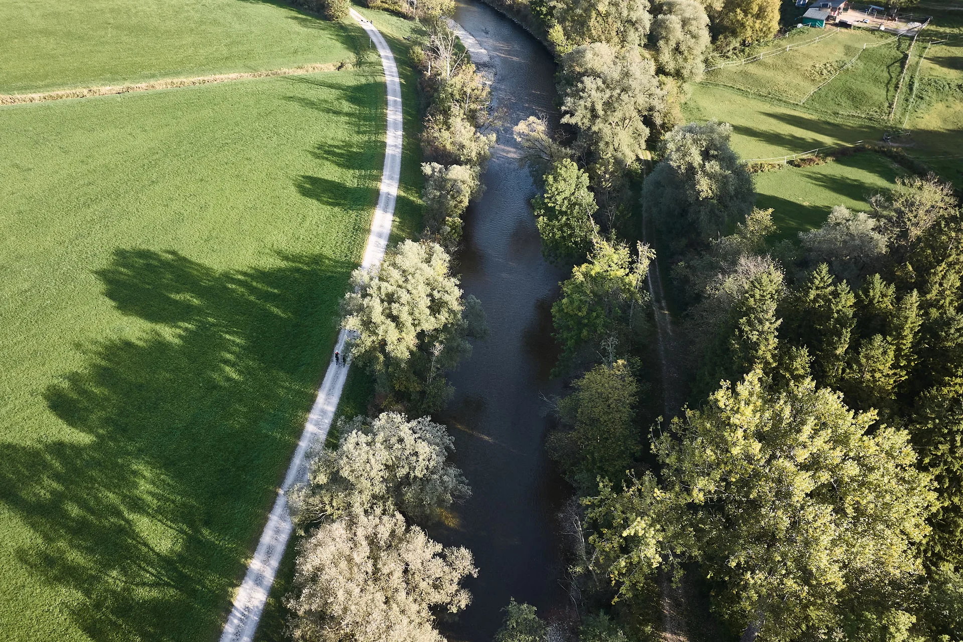 Gravelbike Holidays © Oberbayern.de - Tobias Köhler Luftaufnahme eines Flusses mit Bäumen und einem Weg daneben in einer ländlichen Umgebung