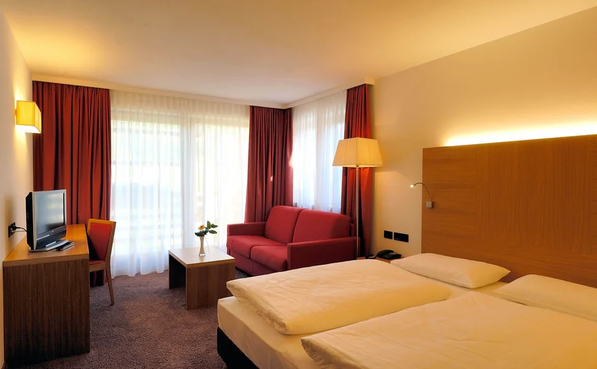 Modernes Hotelzimmer mit Doppelbett, Sofa, Schreibtisch und großem Fenster