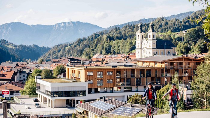 Zwei Radfahrer vor einer Stadt mit Bergen und Kirche im Hintergrund