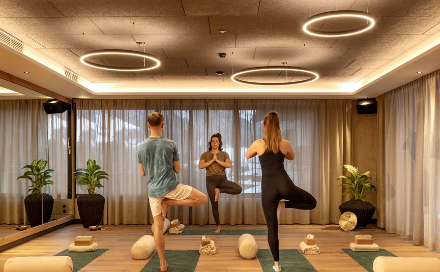 Drei Menschen praktizieren Yoga im Baum-Pose in einem gemütlichen Studio.
