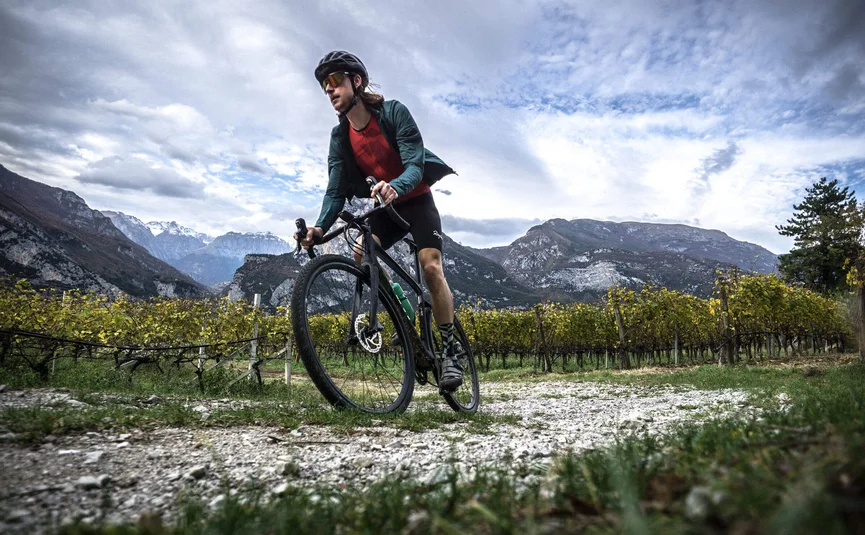 Gravel bike holiday on Northern Lake Garda © Gijs Ferkranus - Wielrenblad Magazine Cyclist riding on gravel path with mountains and vineyards in background