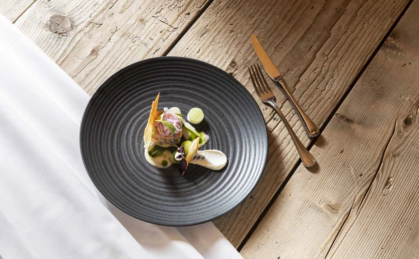 Gourmet dish on black plate with cutlery on rustic wooden table