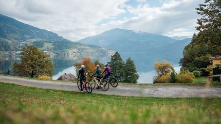 Millstättersee Panoramarunde © Martin Hofmann Drei Radfahrer vor einem See und Bergen an einem bewölkten Tag