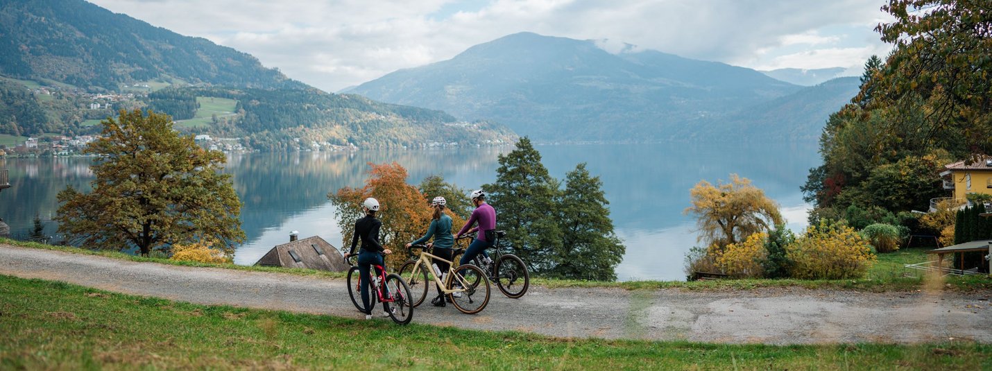 Drei Radfahrer vor einem See und Bergen an einem bewölkten Tag