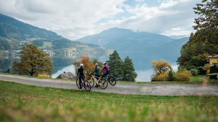 Drei Radfahrer vor einem See und Bergen an einem bewölkten Tag