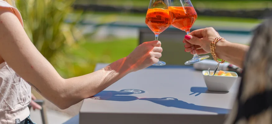 Zwei Personen stoßen mit Orangengetränken im Glas draußen an