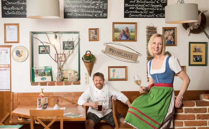 Lächelnder Mann mit Bier und Frau im Dirndl mit Wein in rustikalem Gastraum