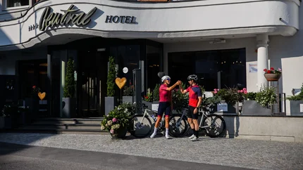 Zwei Radfahrer stoßen vor einem Hotel mit Blumenarrangements an.