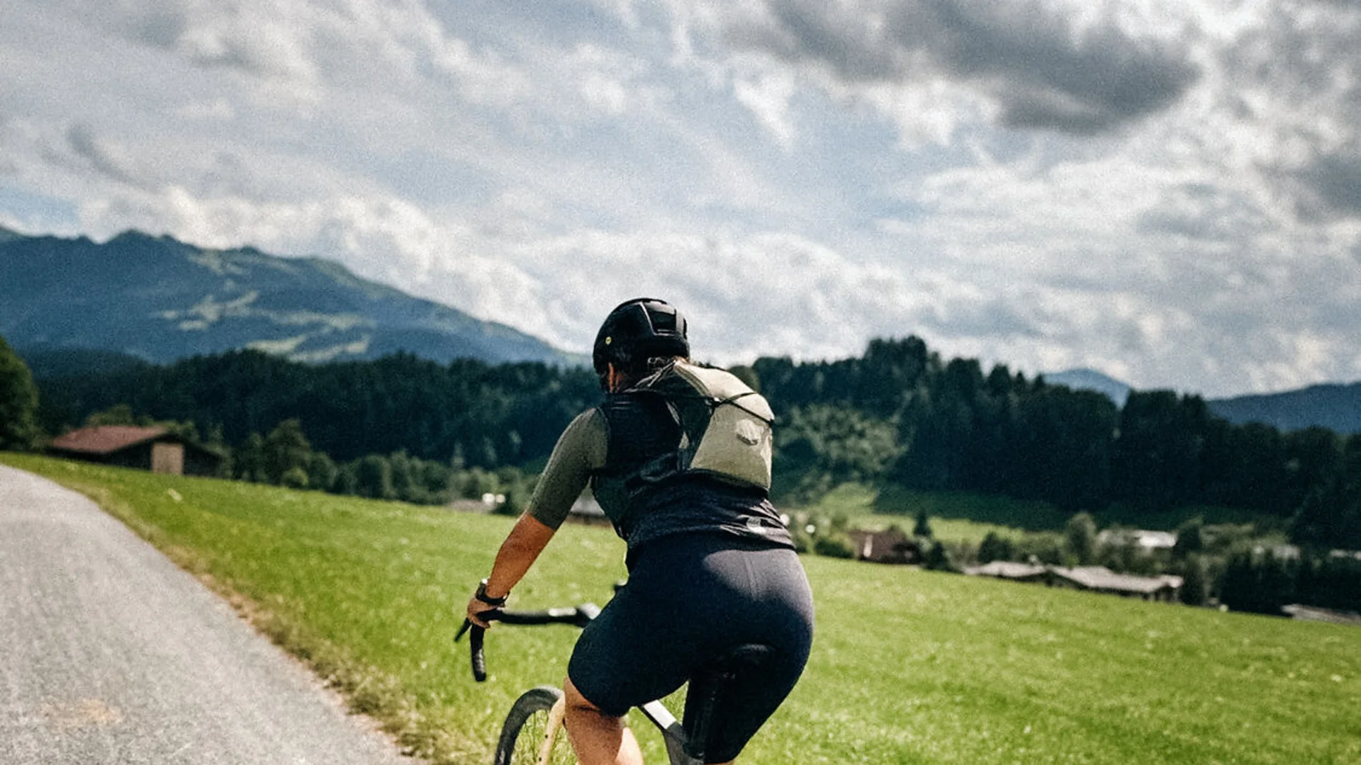 Graveln in den Kitzbüheler Alpen © Martina Wunderle / Flo Distl Fahrradfahrer auf Landstraße mit grünen Wiesen und bewölktem Himmel