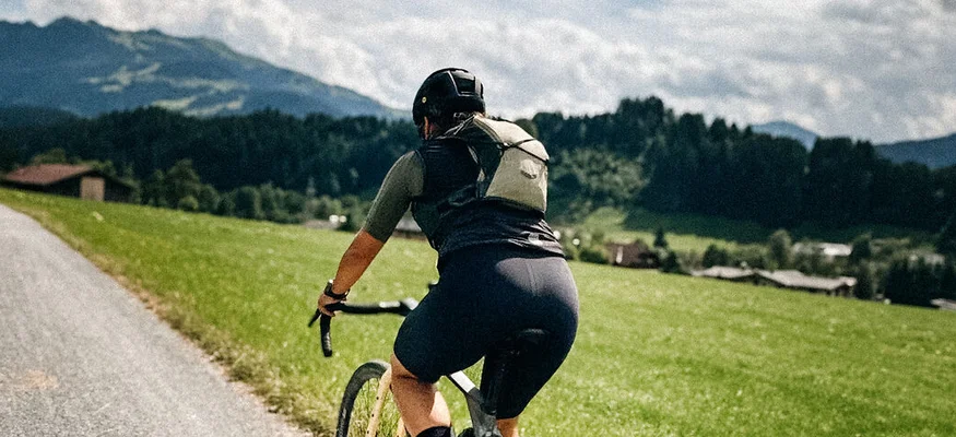 Graveln in den Kitzbüheler Alpen © Martina Wunderle / Flo Distl Fahrradfahrer auf Landstraße mit grünen Wiesen und bewölktem Himmel