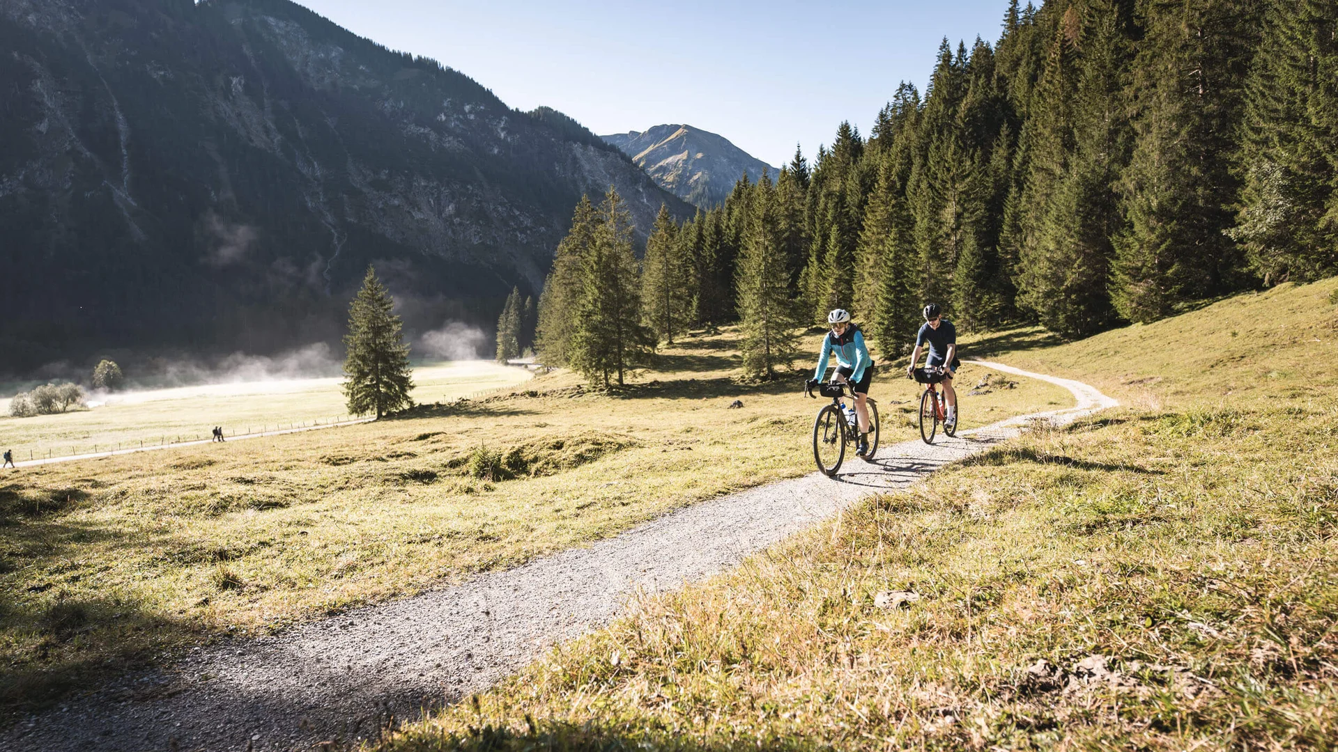 Ride'n Gravel Testival © Andreas Vigl Zwei Radfahrer auf Bergweg vor Wald und Bergen bei sonnigem Wetter