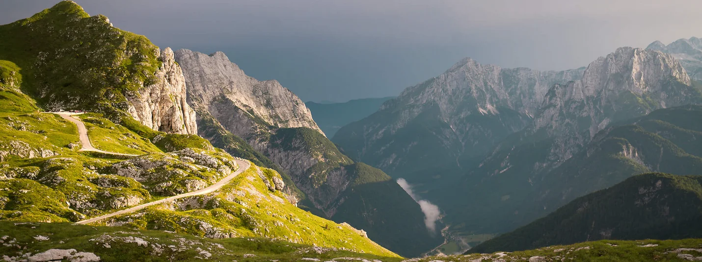 Čez Jelovico v Bohinj © Jessica Dales - www.slovenia.info Gebirgskamm mit kurviger Straße und bewölktem Himmel