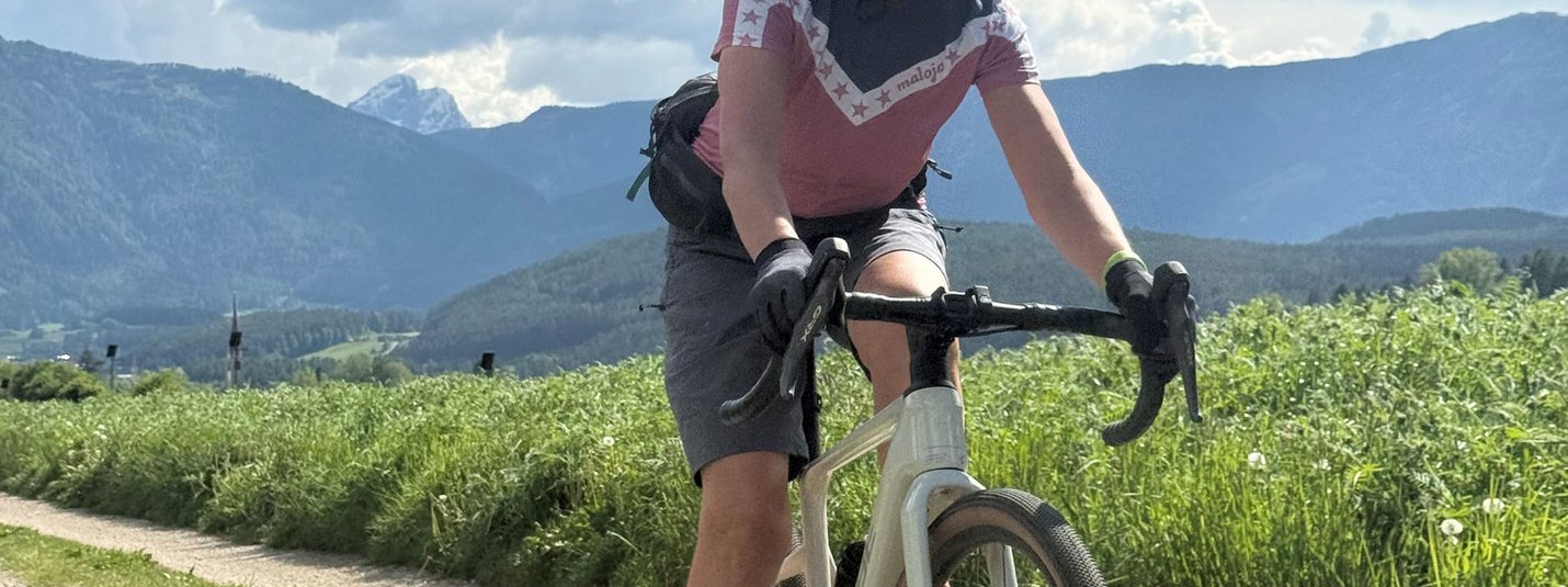 Frau fährt Fahrrad auf Landweg mit Bergen und blauem Himmel im Hintergrund