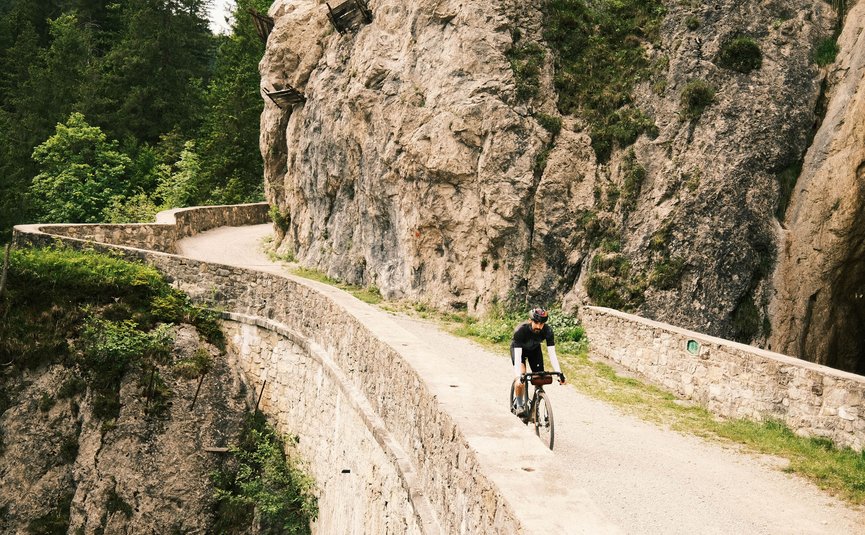 Gravelbike Urlaub in Gravel.Tirol © Liz Kellerer Radfahrer auf einem kurvigen Bergpfad neben einer Felswand