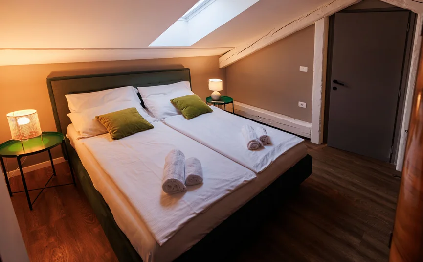 Cozy bedroom with two beds, nightstands, and lamps under sloped ceiling