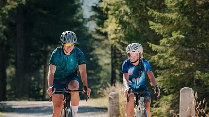 Two cyclists riding on a forest trail in sunny weather