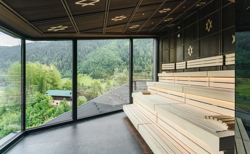 Modern sauna with large glass wall overlooking green mountains