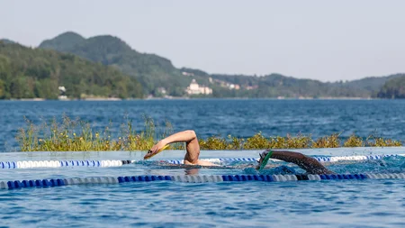 Zwei Schwimmer im Außenpool vor Berg- und Seelandschaft