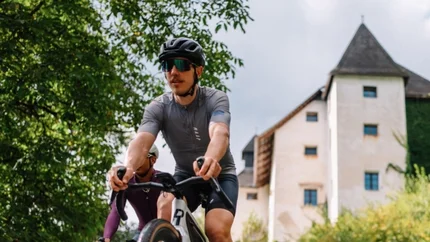Zwei Radfahrer fahren auf einem Weg mit Schloss und grüner Umgebung