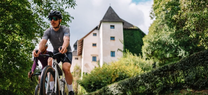 Zwei Radfahrer fahren auf einem Weg mit Schloss und grüner Umgebung