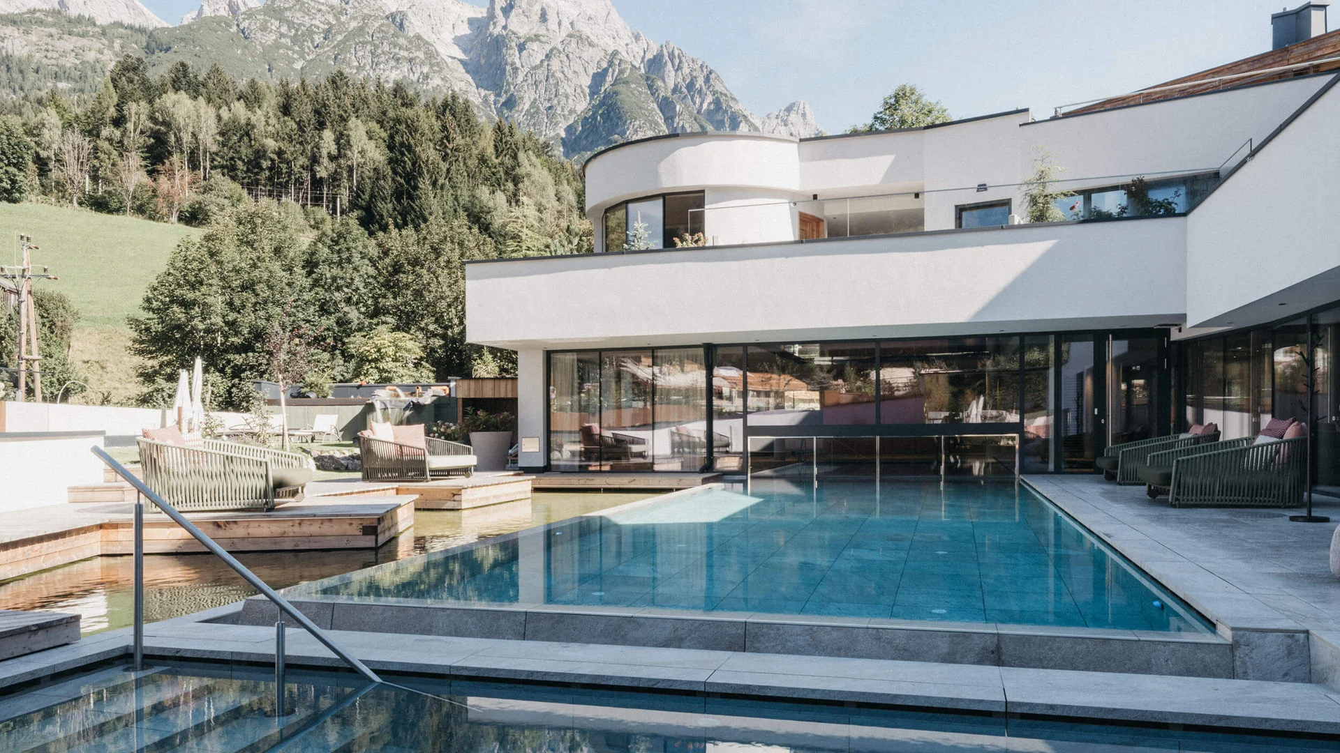 Moderner Pool mit Bergblick vor weißem Haus und Wald