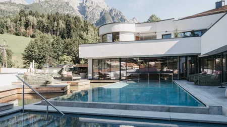 Moderner Pool mit Bergblick vor weißem Haus und Wald