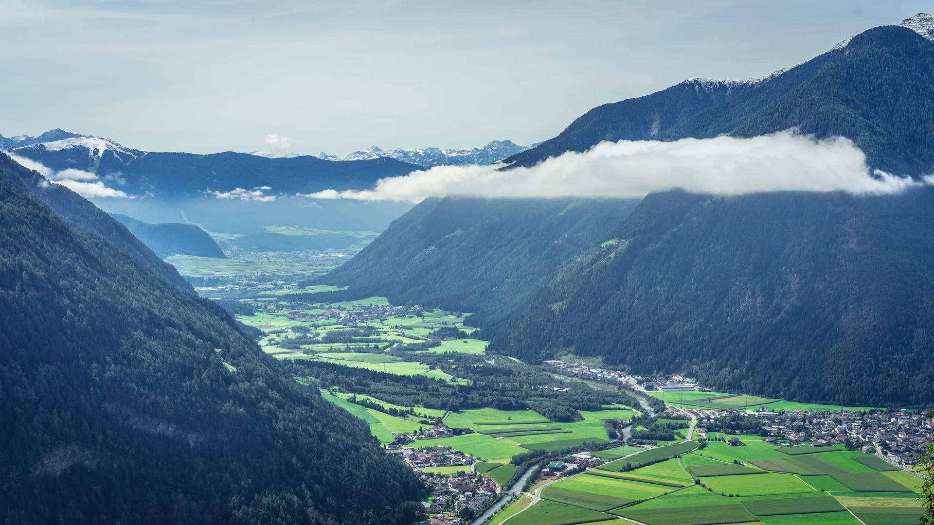 Valley with river, green fields, and forested mountains under clouds