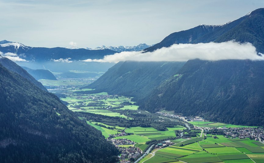 Valley with river, green fields, and forested mountains under clouds