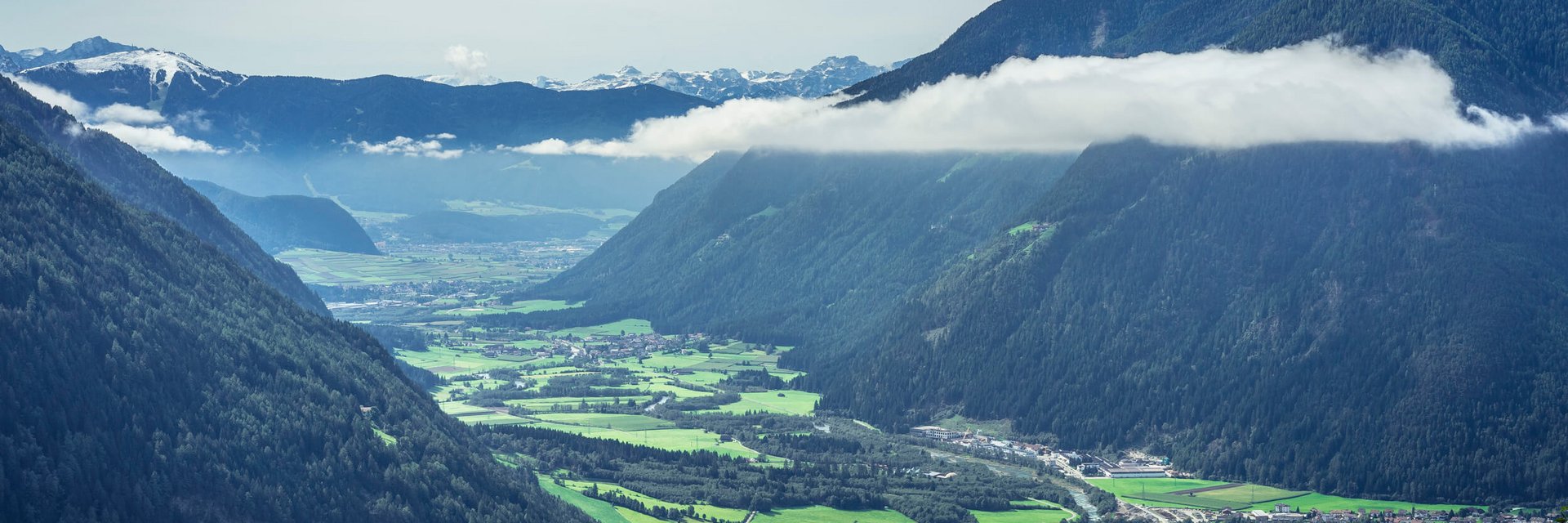 Tal mit Fluss, grünen Feldern und bewaldeten Bergen unter Wolken