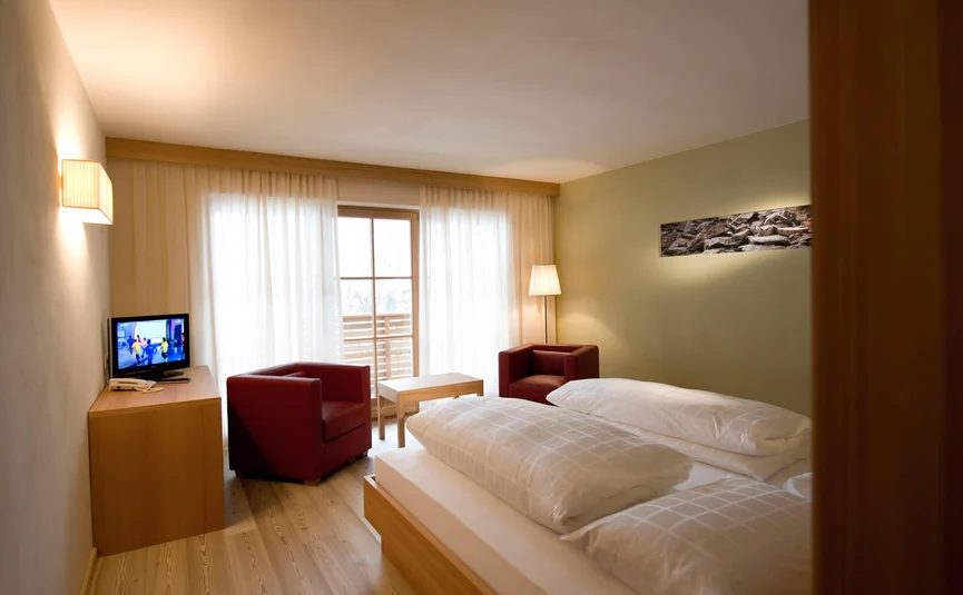 Gemütliches Hotelzimmer mit Doppelbett, zwei roten Sesseln und TV