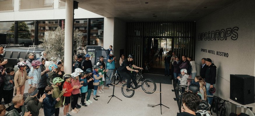Fahrradfahrer zeigt Trick vor applaudierendem Publikum in Sporthotel-Bistro