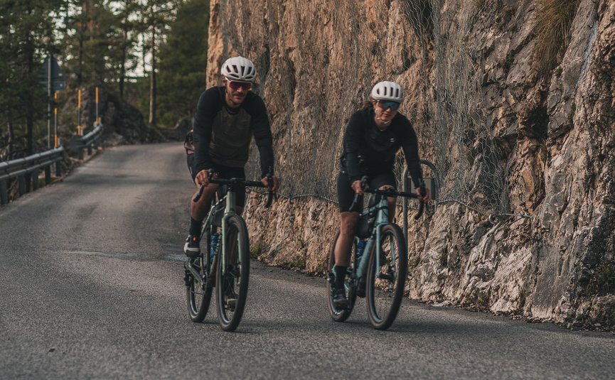 Two cyclists riding on mountain road beside rocky cliff