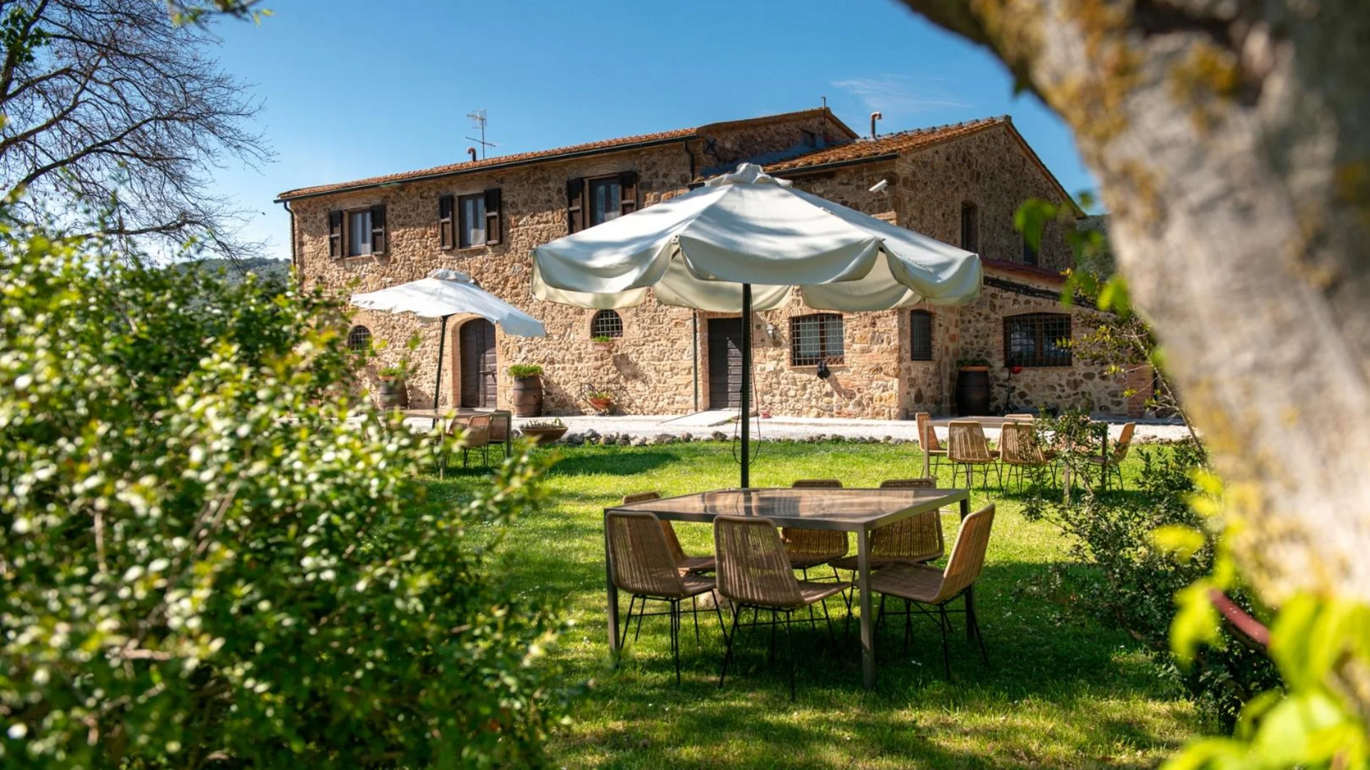 Neue Gravelbike Holidays Hotels 2026 © Tenuta il Cicalino Steinhaus mit Gartenmöbeln und Sonnenschirmen auf grüner Wiese