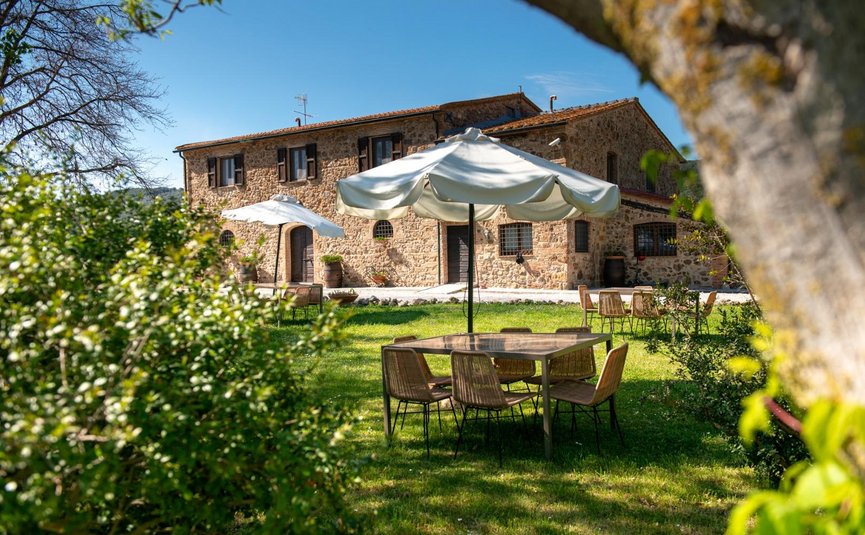 Steinhaus mit Gartenmöbeln und Sonnenschirmen auf grüner Wiese