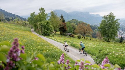 Dornbirn Gravel Tour © Chris Gollhofer - Vorarlberg Tourismus Two cyclists on a path through a blooming spring landscape with mountains