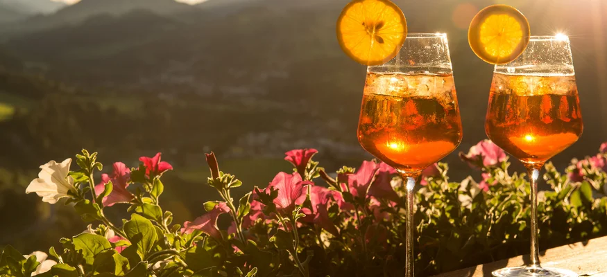 Zwei Aperol Spritz Getränke mit Orangenscheiben vor Berglandschaft