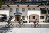 Three cyclists riding past Hotel Jakob on a sunny day
