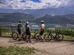Eppan © Heiko Mandl Drei Radfahrer stehen mit ihren Fahrrädern an einem Geländer und blicken auf einen See und Berge.