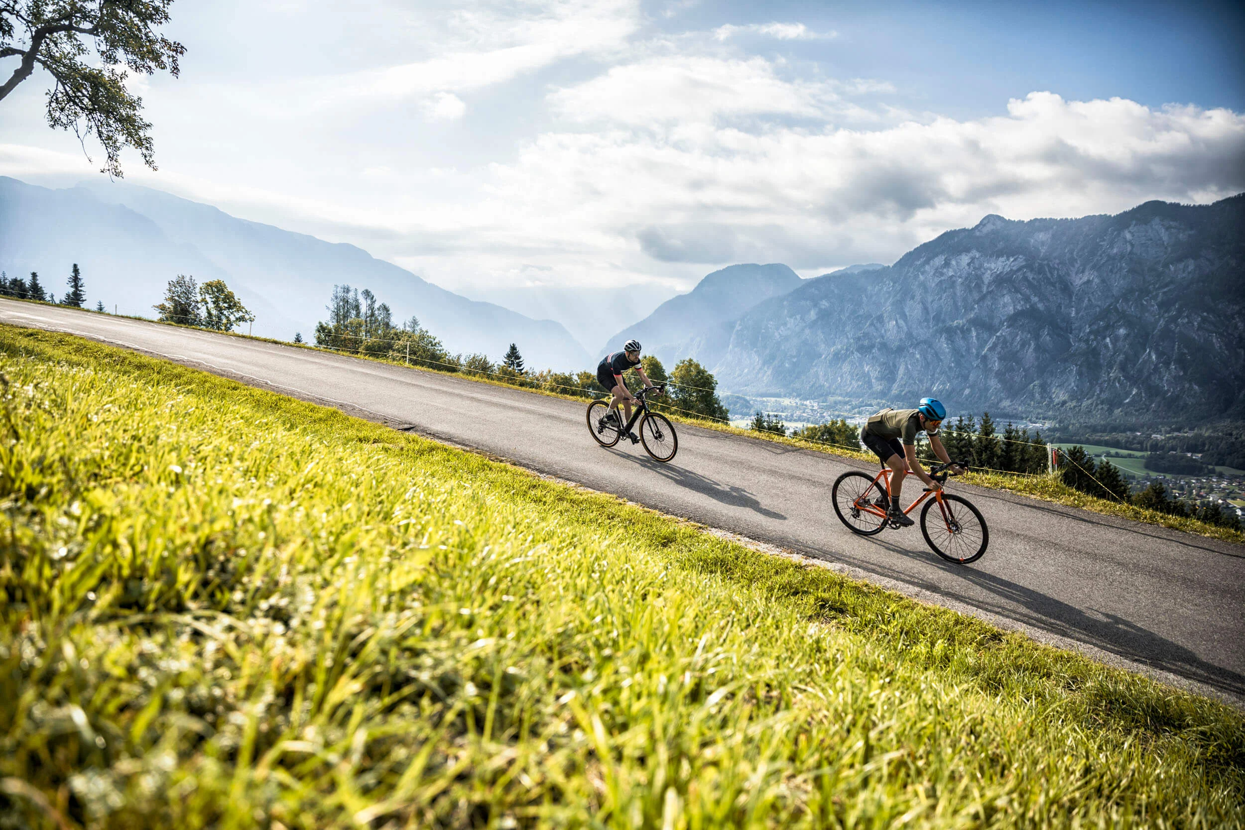 Drei Seen, eine Gravelrunde: Die 3-Seen-Tour ab Fuschl © WOM Medien GMBH - Andreas Meyer Zwei Radfahrer fahren auf einer Straße in bergiger Landschaft bei Tageslicht